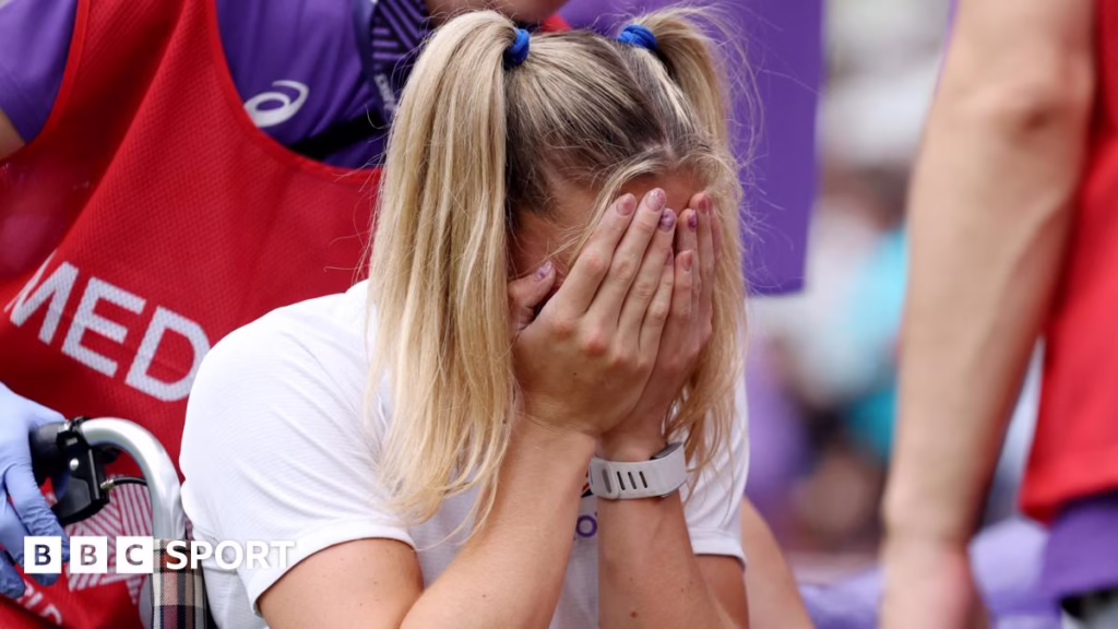 Molly Caudery covers her face with her hands as she's helped away from the track in a wheelchair